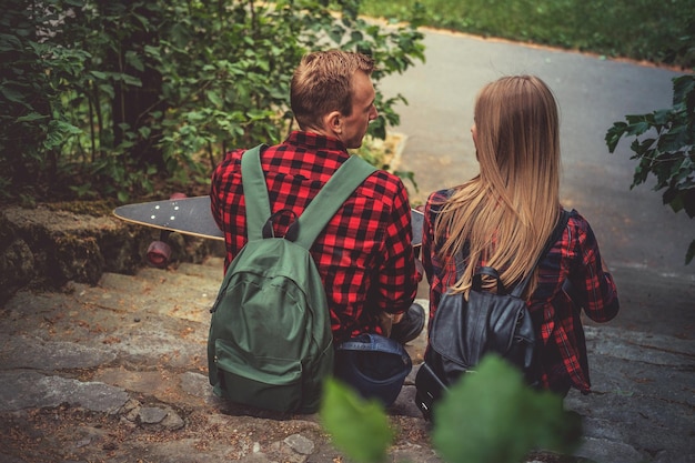 Free photo male in a red shirt with longboard relaxing with his girlfriend on stairway in a park.