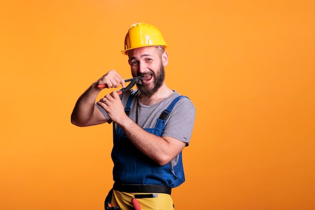 Free photo male restore expert using pair of pliers to repair, working as carpenter or constructor in studio. professional construction worker with hardhat holding pliers and renovating tools on background.