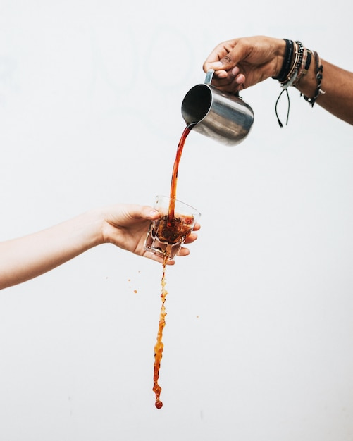 Free photo male's hand pouring a dark liquid into a glass held by a female with a white background