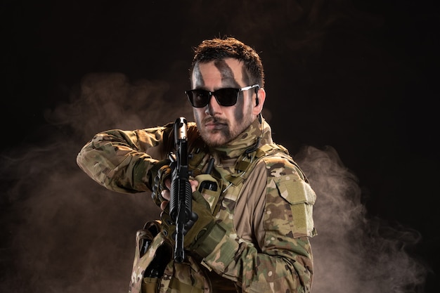 Male soldier in camouflage holding machine gun on a dark wall