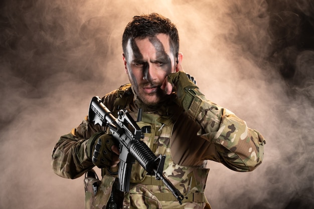 Free photo male soldier in camouflage with machine gun on dark smoky wall