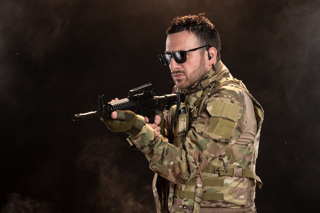 Male soldier in camouflage with machine gun on dark wall