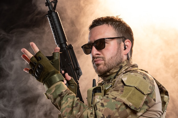 Free photo male soldier in camouflage with machine gun on smoky wall