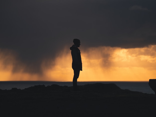 Free photo male standing on a cliff with a yellow and cloudy sky in the background