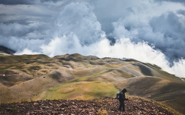 Male standing on a hill covered in greenery under a stormy sky at daytime