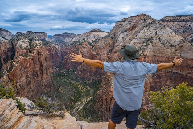 Free photo male standing on top of the rock formations with stretched arms in zion national park, usa