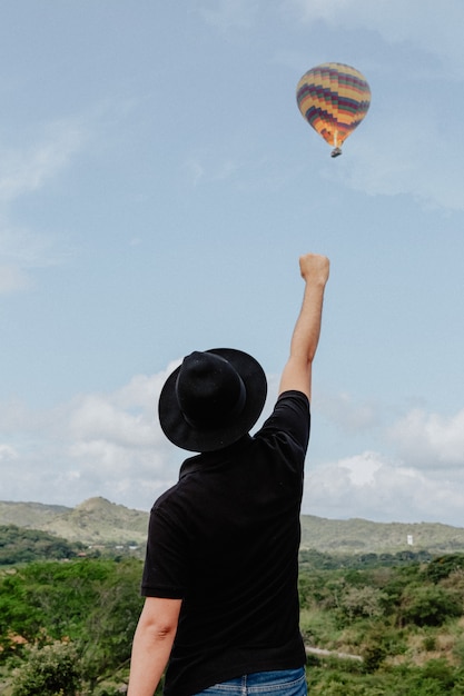 Free photo male standing with his arm and fist raised into the air and a hot air balloon flying the background