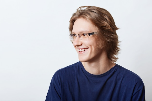 Male student with clever expression having good mood, smiling pleasantly while rejoicing his success at exam. Smiling male enterpreneur in casual t-shirt looking aside with cheerful expression