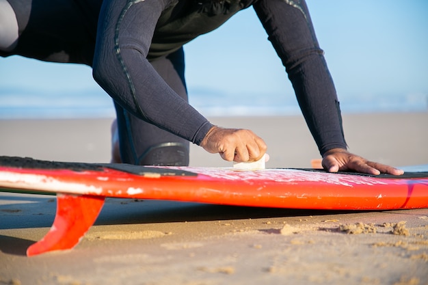 Free Photo male surfer in wetsuit waxing surfboard on sand on ocean beach