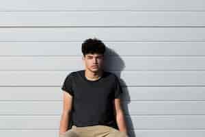 Free photo male teenager sitting and leaning on grey wall