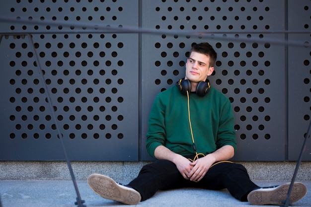 Free Photo male teenager with headphones sitting on floor and leaning back with spread legs