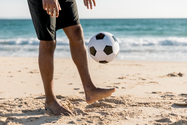 Free photo male tossing ball up playing game on beach