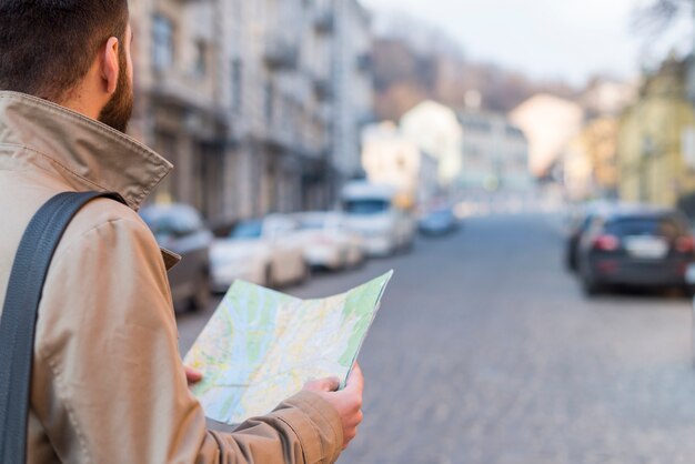 A male traveler holding map in hand finding the way on city street