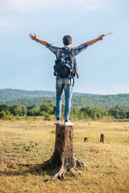 A male traveler with a backpack, carrying a map and standing on a tree stump