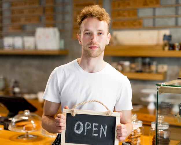 Male waiter holding open sign for coffee shop