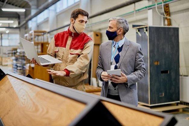 Free Photo male worker using laptop while communicating with company manager at wood factory during coronavirus pandemic