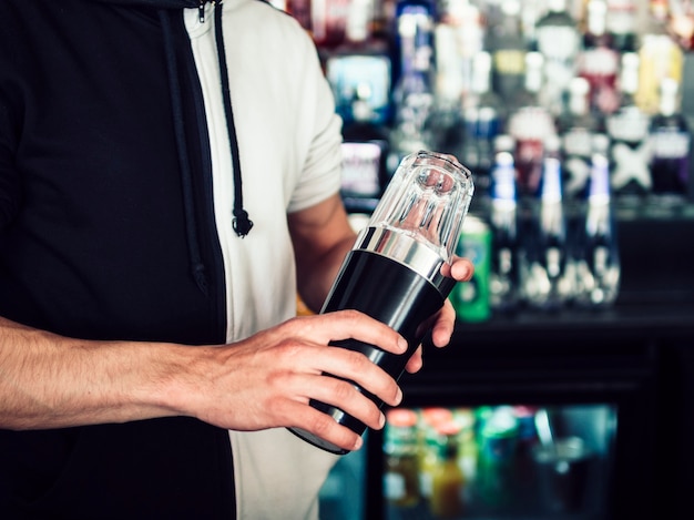 Free photo male young bartender using tumbler to make drink