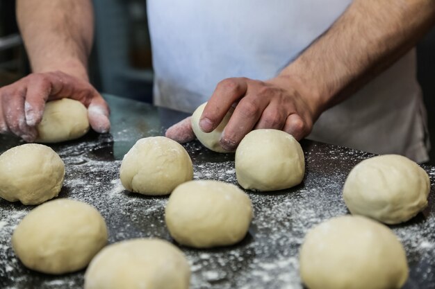 Man are forming dough bolls by two arms flour side view