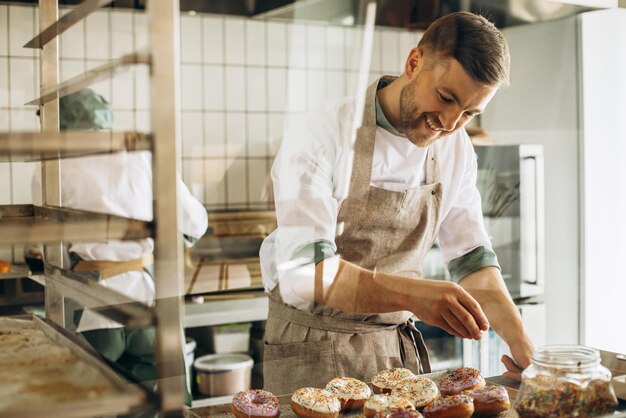 Man baker sprinkles donuts with colorful sweets