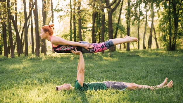 Free photo man balancing woman on his on while practicing yoga in park