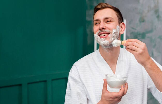 Man in bathrobe applying shaving foam on face with copy space