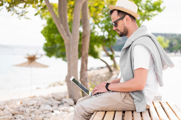 Free photo man at the beach working on laptop