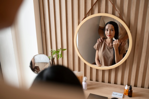 Man being affectionate with woman while she's putting on make-up and looking in the mirror