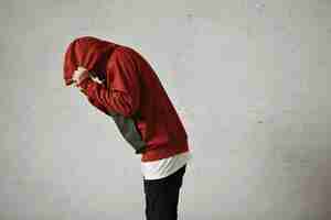 Free photo a man bends down and covers his head with the hood of his red parka, portrait from the side, on white