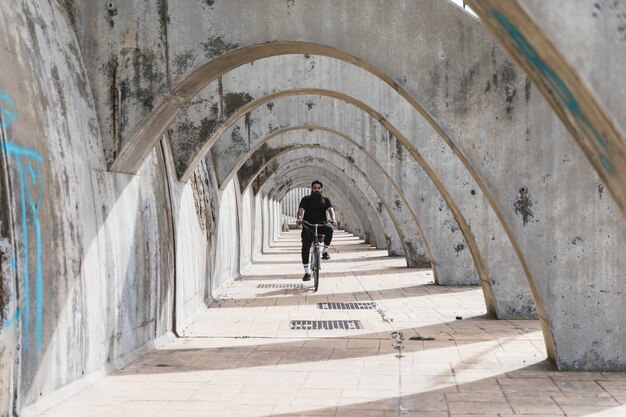 A man in black clothing riding the bicycle in archway