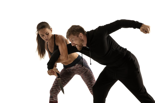 Man in black outfit and athletic caucasian woman fighting on white studio background. Women's self-defense, rights, equality concept. Confronting domestic violence or robbery on the street.