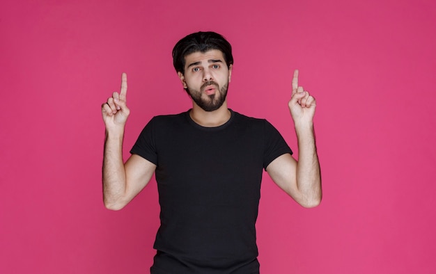 Free Photo man in black shirt with beard pointing at something in a confused manner or showing the direction