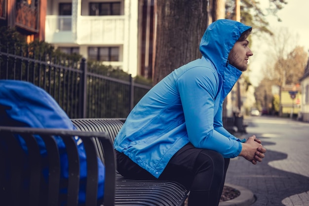 Free Photo a man in a blue hoodie resting on a bench.