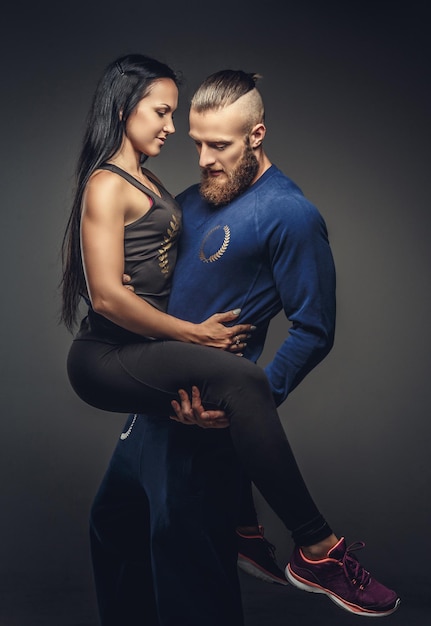 Man in blue sweater holding on arms woman in sportswear. Isolated on grey background.