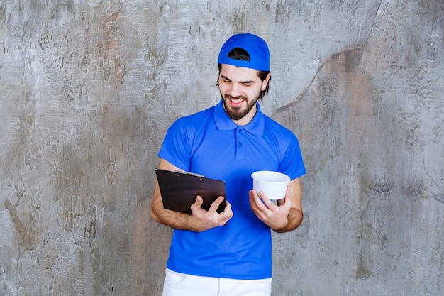 Free photo man in blue uniform holding a takeaway plastic cup and reading the customer name.