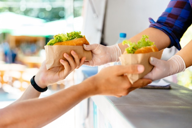 Man buying two hot dog in a kiosk, outdoors. Street food. Close-up view.