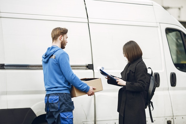 Free Photo man by the truck. guy in a delivery uniform. delivery man with package outdoors