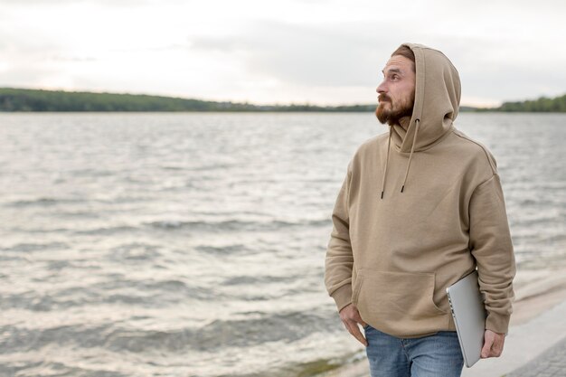 Man carrying laptop next to lake