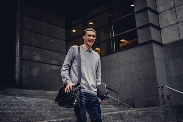 Free Photo man in casual clothes holding laptop and posing on modern street.