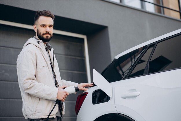 Man charging electric car by the house