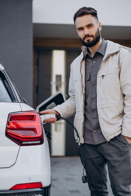 Man charging electric car by the house