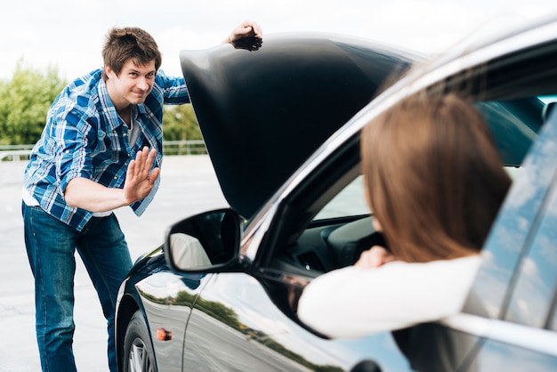 Free Photo man checking engine and woman sitting in car