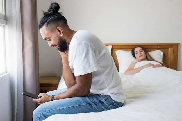 Man checking his phone in bed next to his wife