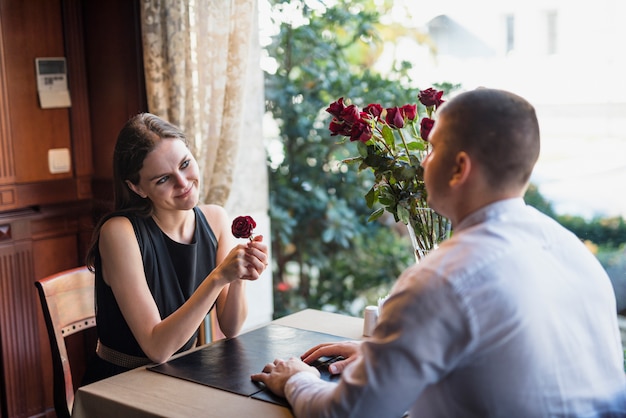 Man and cheerful young woman with flower sitting at table