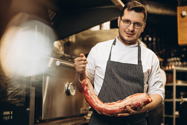 Free photo man chef holding big part of meat at the restaurant kitchen