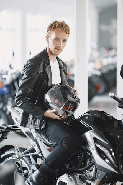 Free photo man choosed motorcycles in moto shop. guy in a black jacket. man in a helmet.