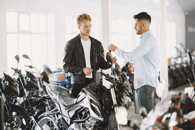 Man choosed motorcycles in moto shop. Guy in a black jacket. Manager with client.