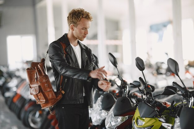 Man choosed motorcycles in moto shop. Guy in a black jacket.