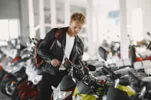 Free photo man choosed motorcycles in moto shop. guy in a black jacket.