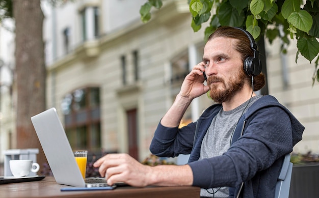 Free photo man at a city terrace working on laptop while wearing headphones