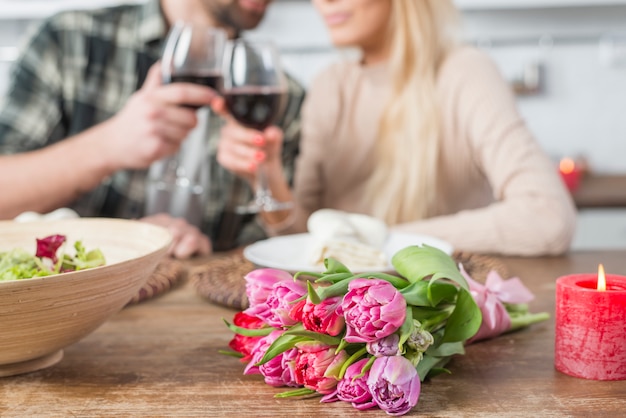 Free photo man clanging glasses with woman at table with flowers and bowl of salad